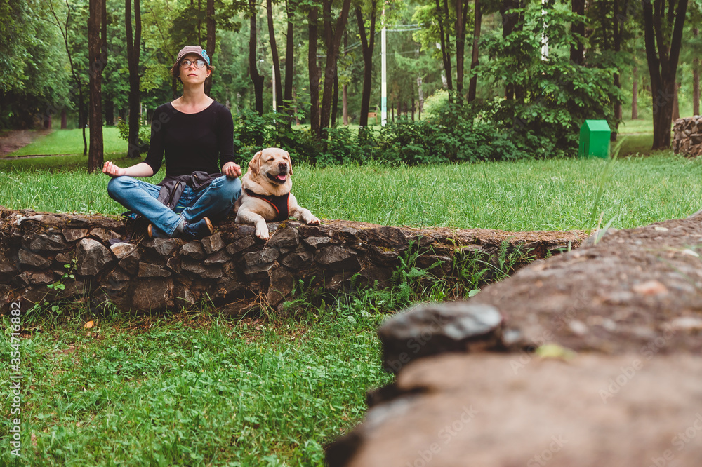 A girl with a dog doing yoga in the Park for a walk. Vacation with a Labrador in nature A girl with a dog doing yoga in the Park for a walk. Vacation with a Labrador in nature