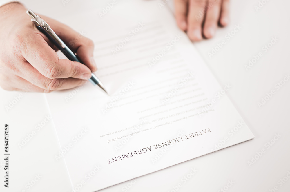 Closeup of a businessman signing an Patent License Agreement contract with a pen. Closeup of a businessman signing an Patent License Agreement contract with a pen.