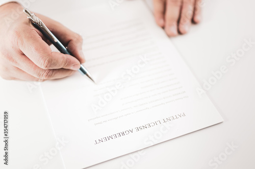Closeup of a businessman signing an Patent License Agreement contract with a pen.