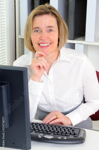 Happy Middle Aged Caucasian Fifty Year Old Woman Working In An Office With A Computer Sat At A Desk