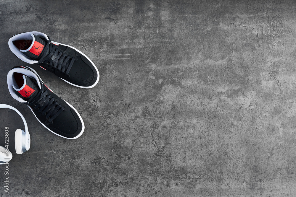 krave panik nå VIENNA, AUSTRIA - MAY 10, 2019: Nike Air Jordan 1 Mid black, grey, red and  white sneakers and white wireless Beats headphones on dark concrete  background. Top view. Stock Photo | Adobe Stock