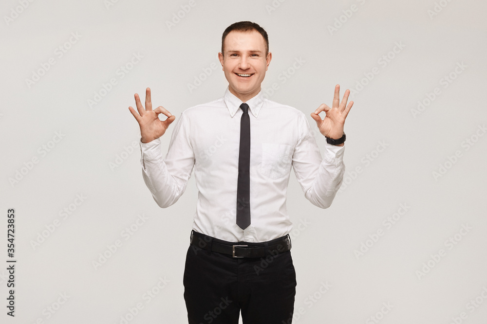 Handsome smiling businessman in a white shirt and black tie showing an ok sign with fingers over white background, isolated. Advertise mockup Handsome smiling businessman in a white shirt and black tie showing an ok sign with fingers over white background, isolated. Advertise mockup