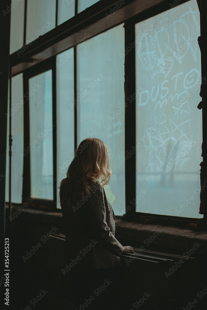 The young woman watching out of the window in an abandoned factory located in Saint Petersburg, Russia. The young woman watching out of the window in an abandoned factory located in Saint Petersburg, Russia.