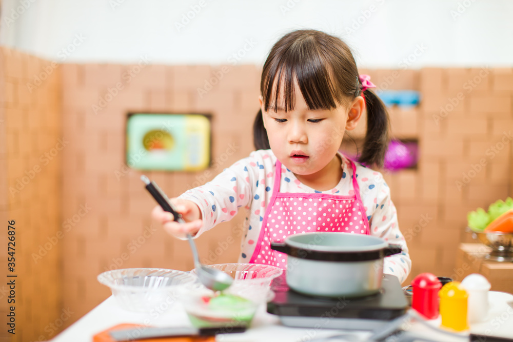 toddler girl pretend play food preparing role against cardboard blocks kitchen background toddler girl pretend play food preparing role against cardboard blocks kitchen background