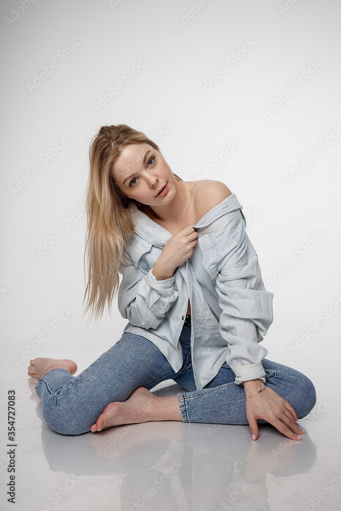 portrait of sexy caucasian woman with long hair posing in blue shirt and jeans on white studio background. model tests of pretty girl in basic clothes. attractive female sitting on floor on her knees portrait of sexy caucasian woman with long hair posing in blue shirt and jeans on white studio background. model tests of pretty girl in basic clothes. attractive female sitting on floor on her knees