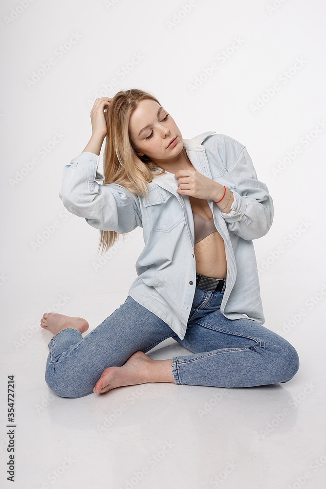 portrait of sexy caucasian woman with long hair posing in blue shirt and jeans on white studio background. model tests of pretty girl in basic clothes. attractive female sitting on floor on her knees portrait of sexy caucasian woman with long hair posing in blue shirt and jeans on white studio background. model tests of pretty girl in basic clothes. attractive female sitting on floor on her knees