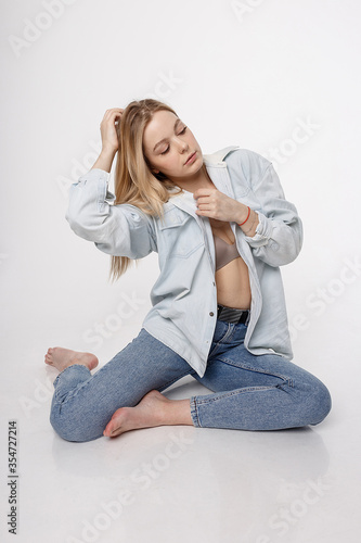 portrait of sexy caucasian woman with long hair posing in blue shirt and jeans on white studio background. model tests of pretty girl in basic clothes. attractive female sitting on floor on her knees