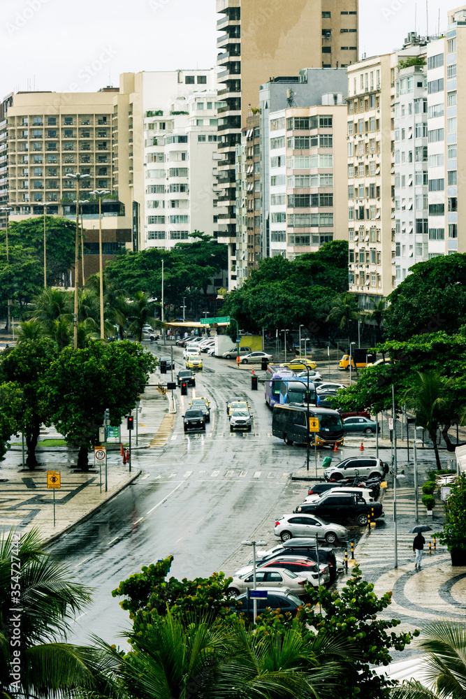 Rainy intersection showing cars and tour buses surrounded by trees, apartments, and hotels.