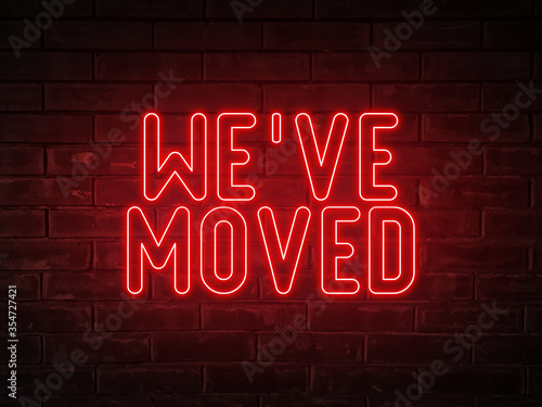 We've moved - red neon light word on brick wall background