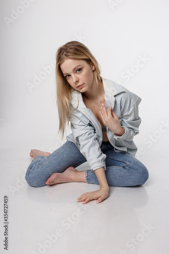 portrait of sexy caucasian woman with long hair posing in blue shirt and jeans on white studio background. model tests of pretty girl in basic clothes. attractive female sitting on floor on her knees