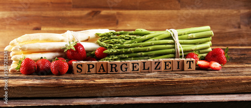 White and green asparagus and strawberries on background with the german word Spargelzeit in wooden letter.