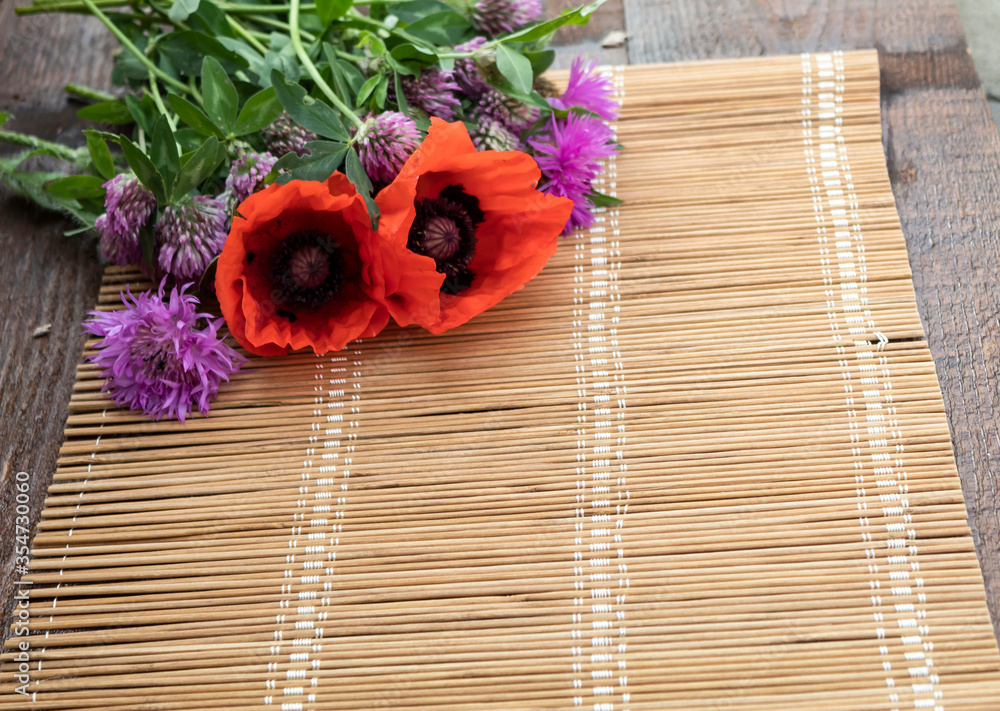 Against the background of straw napkins in the corner is a bouquet of poppy flowers, cornflowers and clover.