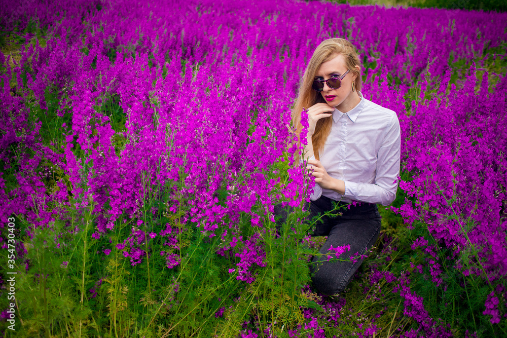 blonde in sunglasses and a white shirt on the field with purple flowers blonde in sunglasses and a white shirt on the field with purple flowers