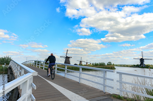 Wallpaper Mural Outdoor sport, man rides a bicycle on old woden bridge, windmills in dutch landscape, Kinderdijk in South Holland, Netherlands Torontodigital.ca