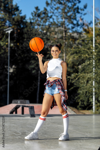Fit brunette modern young woman posing with basket ball at the skatepark.