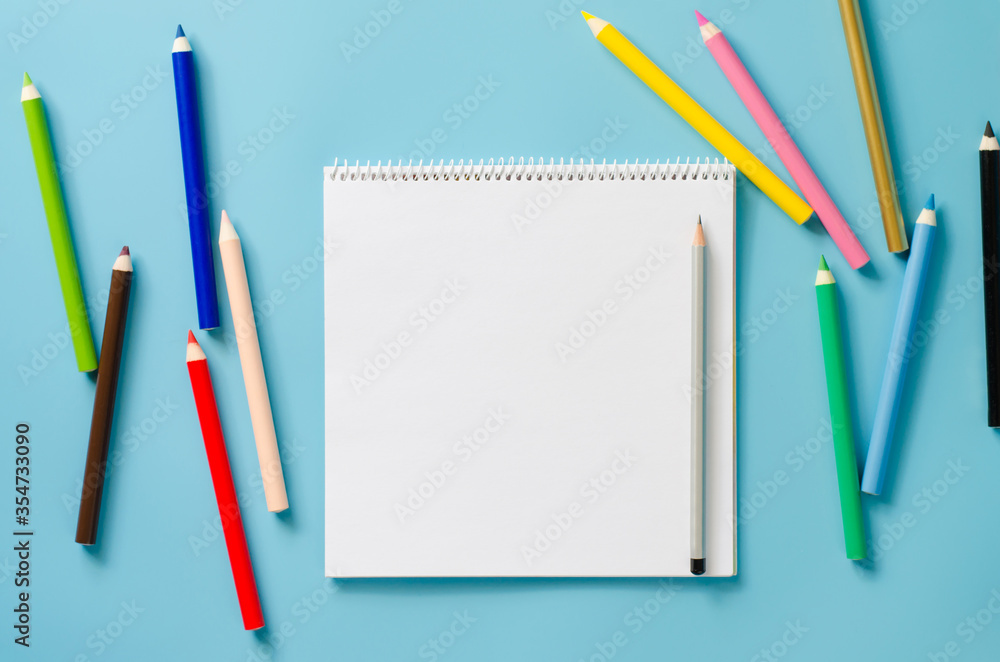 Empty square notebook and set of colorful pencils on blue background. Blank paper. Empty square notebook and set of colorful pencils on blue background. Blank paper.