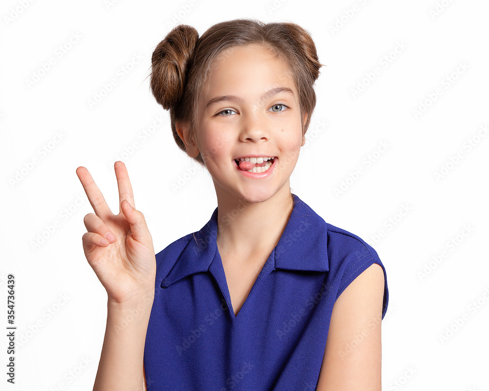 Funny girl. A beautiful European teen girl in a blue dress on a white background makes a funny face, shows her hand the sign V. Face for advertising. Young skin without makeup.