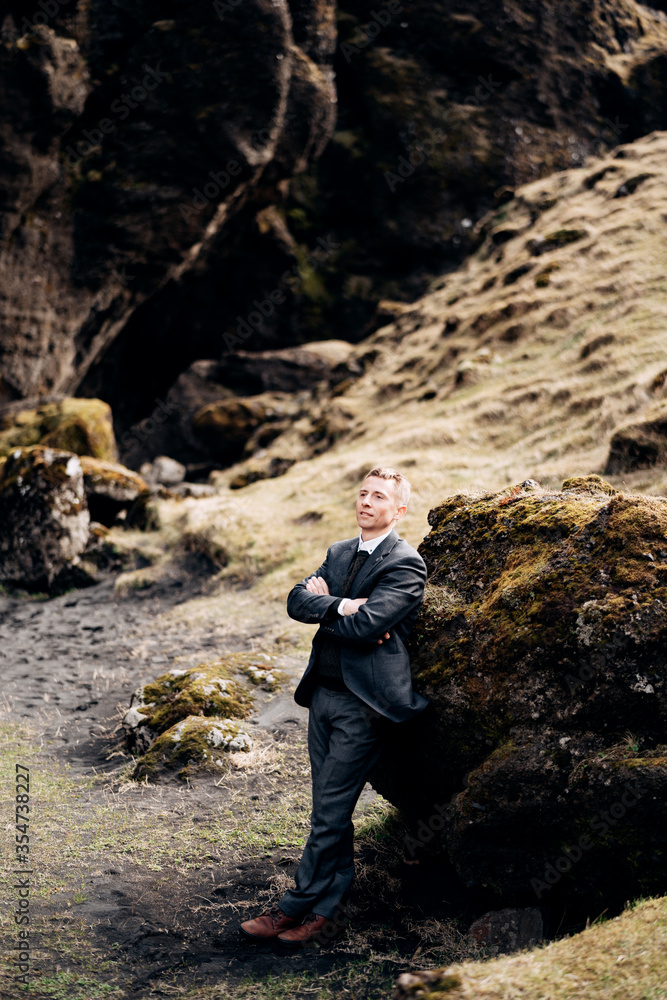 Portrait of a groom leaning on a stone in a moss, next to a rocky cleft with a mountain river. Destination Iceland wedding. 