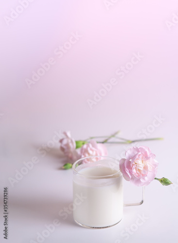 glass of milk on white table with soft pink flowers. elegant pink carnation flowers in pastel colours