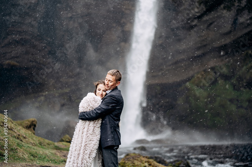 Destination Iceland wedding, near Kvernufoss waterfall. Wedding couple is standing near the waterfall. The groom hugs the bride.