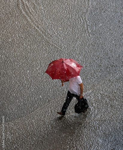 businessman in a very heavy rain walks down the street. is holding bag and red umbrella in hand. 