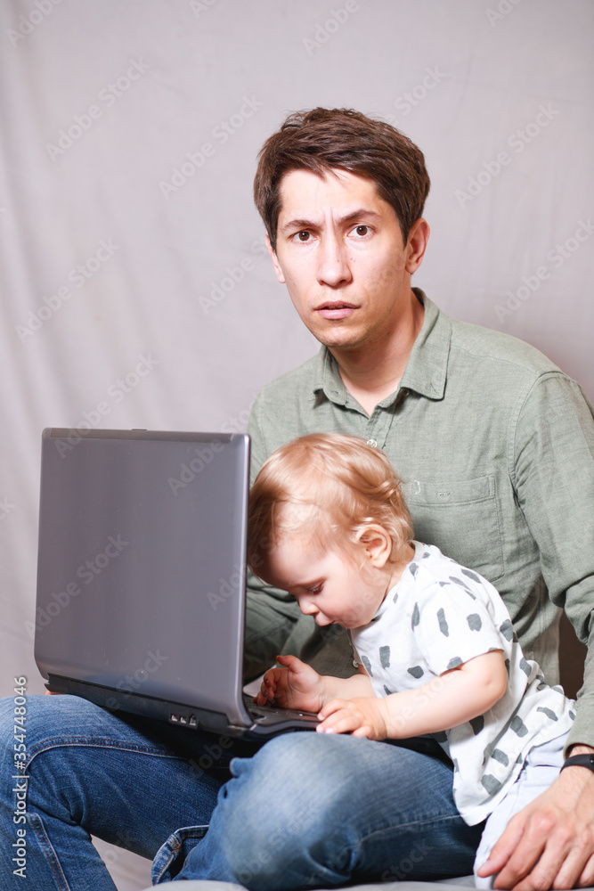 © Aleksei Zakharov - young man working at home with a laptop with a baby on his hands. Stay home concept. Home office with kids. © Aleksei Zakharov - young man working at home with a laptop with a baby on his hands. Stay home concept. Home office with kids.