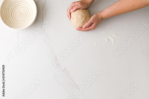 Top view of female hand molding bread dough in a marble table with an empty bread bowl with space for text