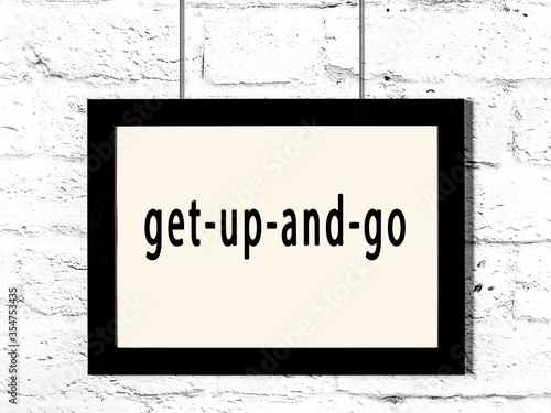 Black frame hanging on white brick wall with inscription get-up-and-go