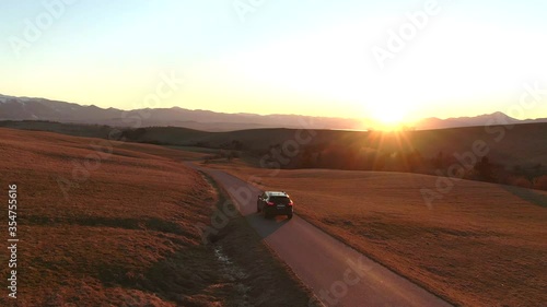 4K aerial drone shot sun flare - lonely car in empty road on the way for a vacation to the lake during a beautiful sunset from bird's perspective - nice landscape