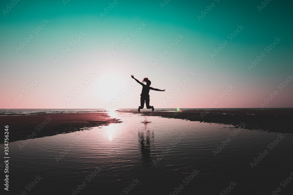 silueta de mujer saltando en la playa al atardecer