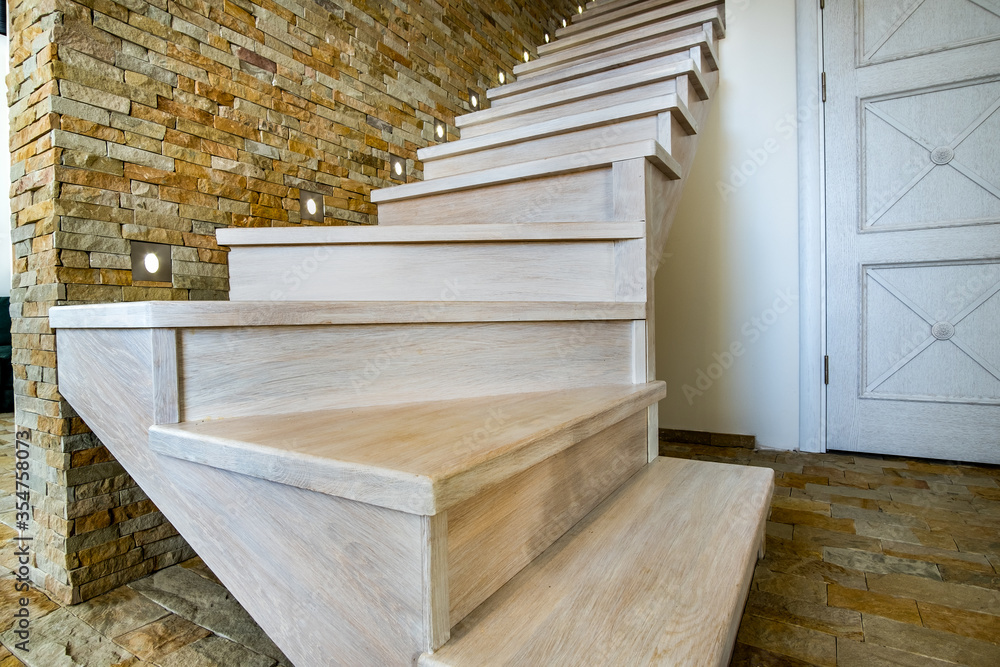 Stylish wooden contemporary staircase inside loft house interior. Modern hallway with decorative limestone brick walls and white oak stairs. Stylish wooden contemporary staircase inside loft house interior. Modern hallway with decorative limestone brick walls and white oak stairs.