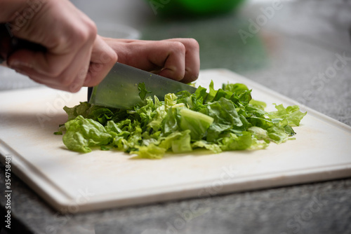 hands cutting lettuce with knife on white table on kitchen counter
