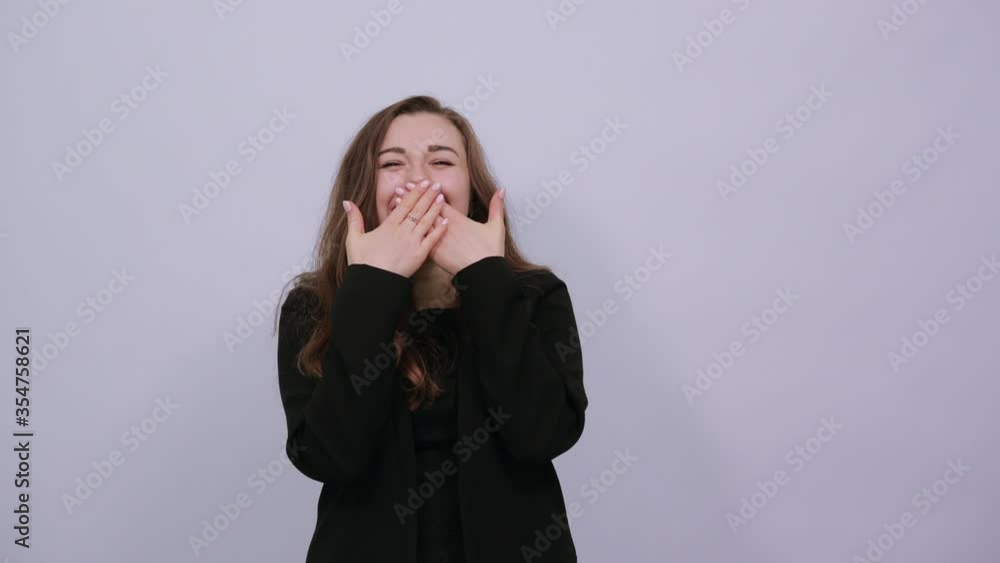 Covering her mouth with hand and gazing while giggling expresses sincere emotions of joy cheerful mood, portrait. Young attractive woman brunette in a black t-shirt, sweater on white background Covering her mouth with hand and gazing while giggling expresses sincere emotions of joy cheerful mood, portrait. Young attractive woman brunette in a black t-shirt, sweater on white background