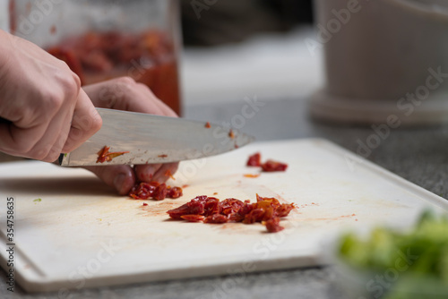 hands cutting dried tomato with knife on white table on kitchen counter