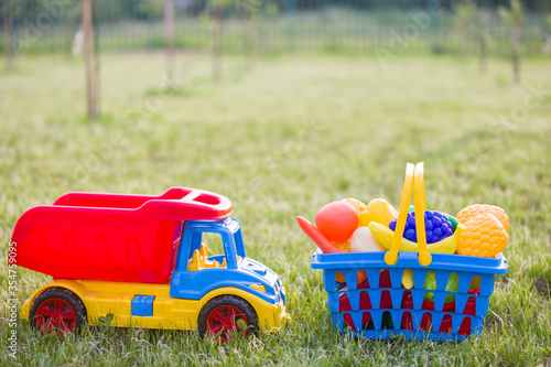 Car truckand a basket with toy fruit and vegetables. Bright plastic colorful toys for children outdoors on sunny summer day. photo