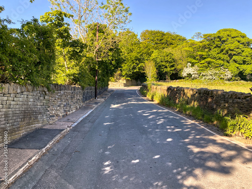 A country lane on a sunny evening, with trees and dry stone walls in, Shibden Valley, Halifax, UK