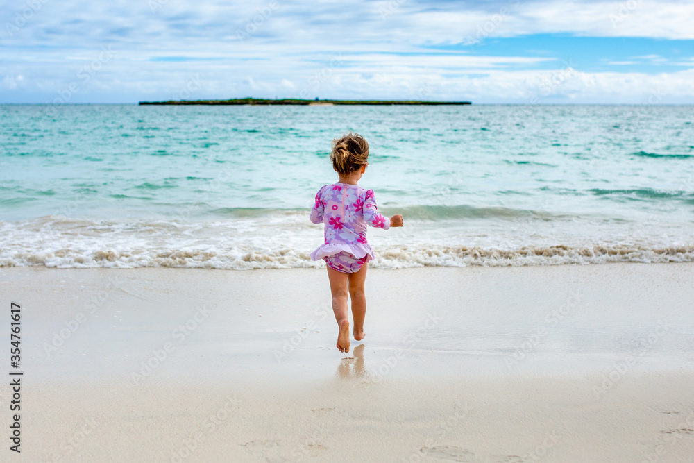 Young girl in flower swimsuit runs down beach to the ocean Young girl in flower swimsuit runs down beach to the ocean