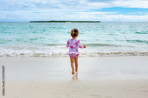 Young girl in flower swimsuit runs down beach to the ocean