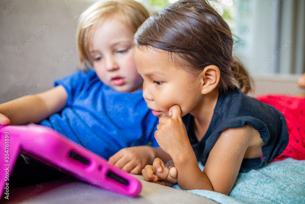 Caucasian boy and Asian girl play and learn on electronic tablet device Caucasian boy and Asian girl play and learn on electronic tablet device