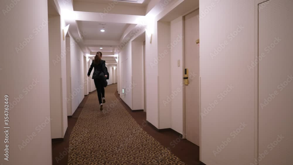 Happy woman jump and bounce, skippingly run along empty passage of hotel. Lady wear black formal suit, swing hand with laptop bag Happy woman jump and bounce, skippingly run along empty passage of hotel. Lady wear black formal suit, swing hand with laptop bag