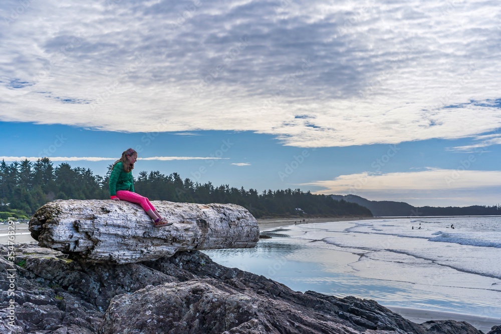 girl sitting on huge driftwood log on the beach in Tofino, Vancouver island, British Columbia, Canada 