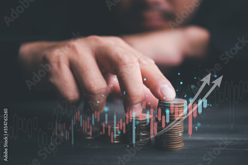 Investment business Finance concept.Money management and Financial chart. Businessman is touching a growing virtual hologram stock and rows of coins on dark tone background.Business stock analysis.