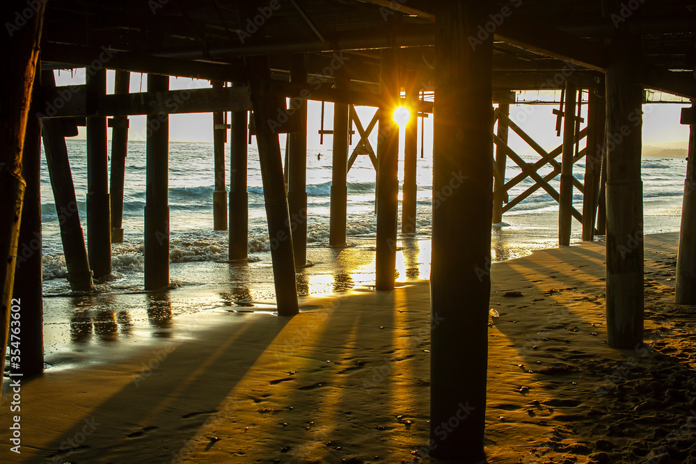 Sunset from under a pier with surf sand waves and surfers out in the water