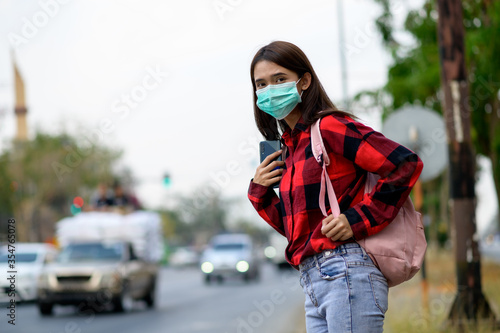 Asian teenage woman wearing Mark stands on the roadside of a city car.