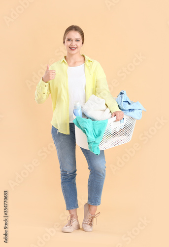 Young woman with laundry showing thumb-up gesture on color background