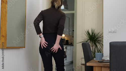 Young tall woman feels sudden pain in the anus caused by hemorrhoids, touches her buttocks. Medium shot photo