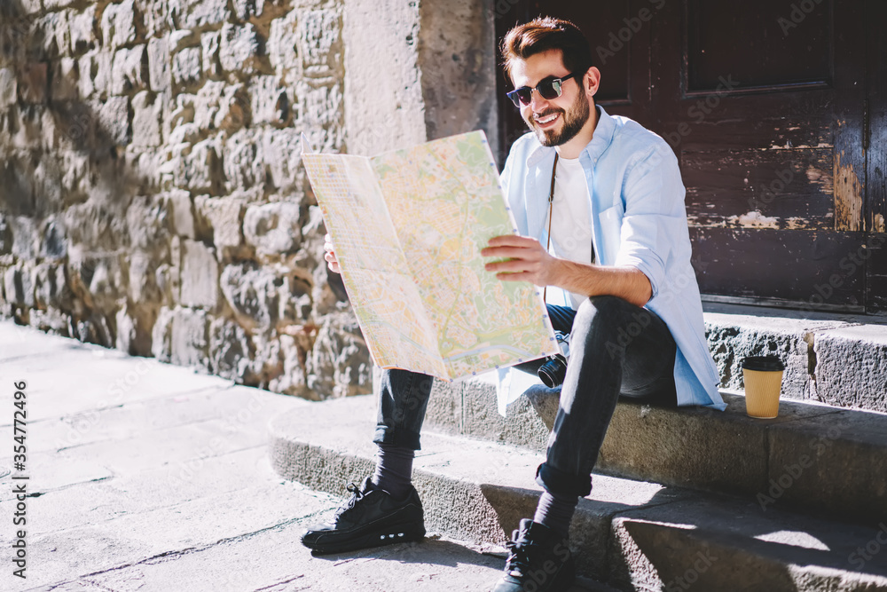 Positive hipster guy in casual wear resting on old stairs during sightseeing tour in city Positive hipster guy in casual wear resting on old stairs during sightseeing tour in city