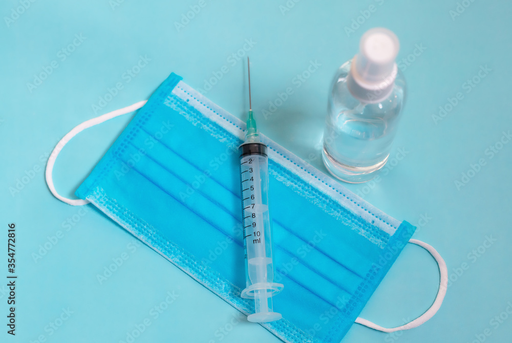 Bottle of hand sanitizer, syringe, antimicrobial liquid spray, germ prevention or antibacterial hygiene. Medical mask, Medical protective masks on blue background. Blue medical disposable face mask Bottle of hand sanitizer, syringe, antimicrobial liquid spray, germ prevention or antibacterial hygiene. Medical mask, Medical protective masks on blue background. Blue medical disposable face mask