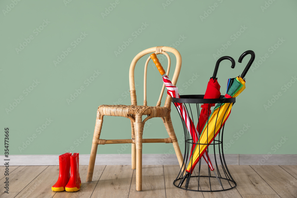 Umbrellas, chair and gumboots near color wall