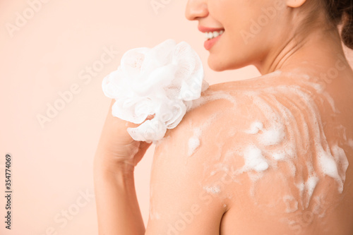 Beautiful young woman taking shower on color background